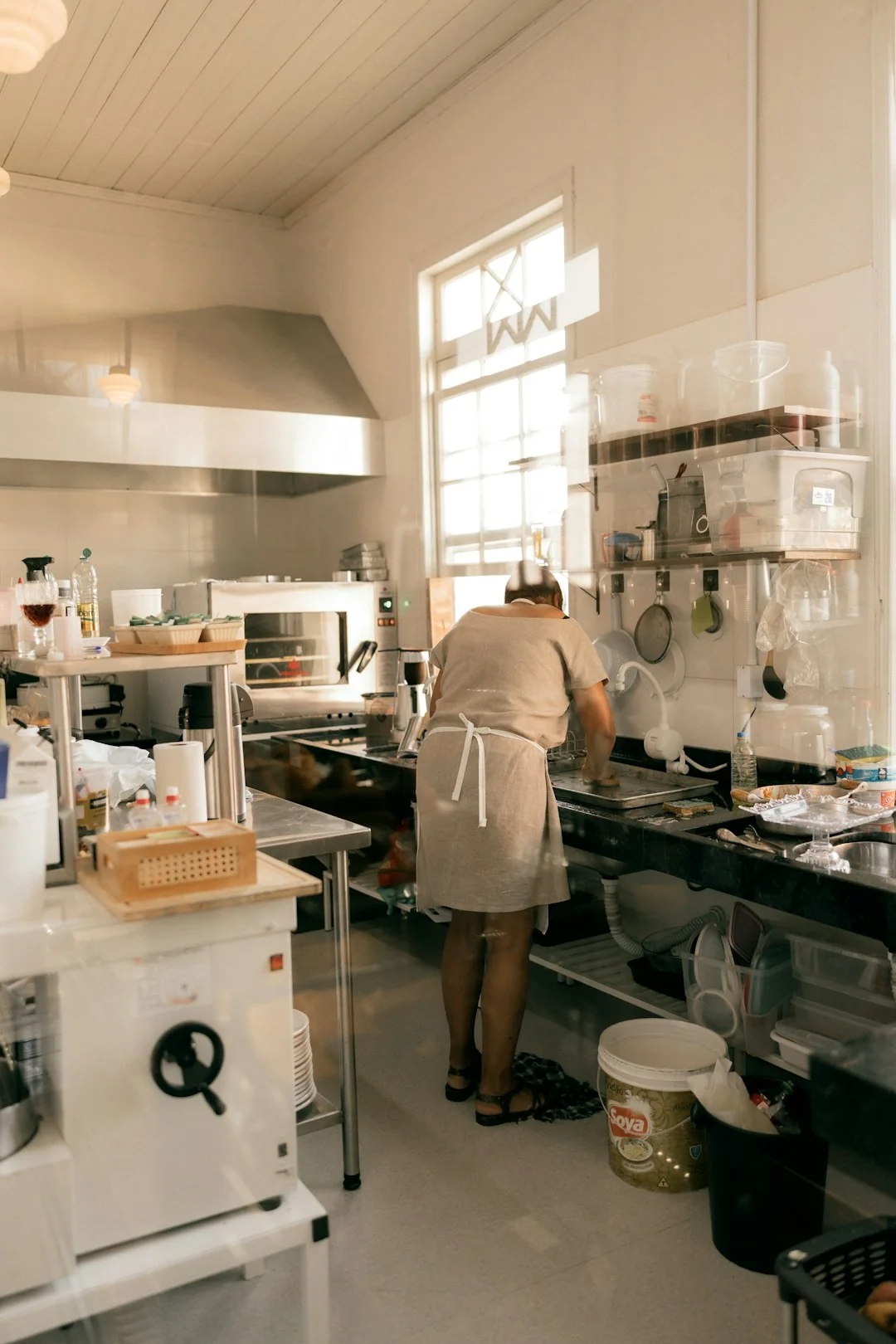 A woman carefully wraps a sofa in protective material while packing boxes in a bright room.